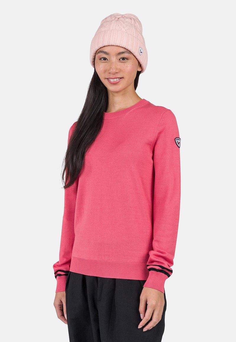 Różowy sweter z dzianiny z długimi rękawami, prążkowanymi mankietami i dołem. Czarny i biały pasek na mankietach. Nosi się z jasnoróżowym czapką w warkocze.