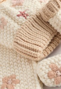 Strikkede uldsaccessories i creme og tan, med blomsterbroderi i bløde pastelfarver, samt en kraftig ribbet tekstur.