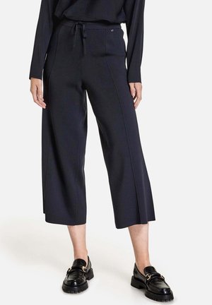 Pantalons crop en bleu marine foncé en tissu doux, avec une taille à cordon de serrage et des détails sur les côtés, associés à des mocassins à plateforme noirs.
