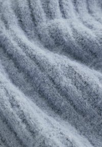 Mjukt, ljusblått stickat tyg med en texturerad, fluffig yta. Innehåller vertikalt ribbad struktur och en lös, bekväm väv.