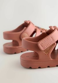 Pink open-toe sandals with a textured upper, adjustable strap, and a cushioned sole. Includes decorative accent details.