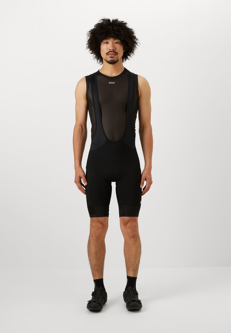 Black cycling bib shorts with mesh upper, form-fitting design, shorts reach mid-thigh, features minimalistic logo on chest.