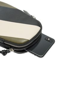 Kieszonka zapinana na zamek w czerni, zieleni i kremowej skórze; charakteryzuje się eleganckim designem z częściowo włożonym smartfonem. Gładka tekstura, minimalny sprzęt.