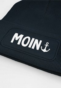 Navy beanie hat featuring a textured ribbed design and a patch with the word "MOIN" and an anchor icon in white.