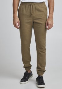 Pantalones jogger color caqui con cintura elástica, detalle de cordón y piernas ajustadas; combinados con zapatillas negras. Tejido suave y ligero.