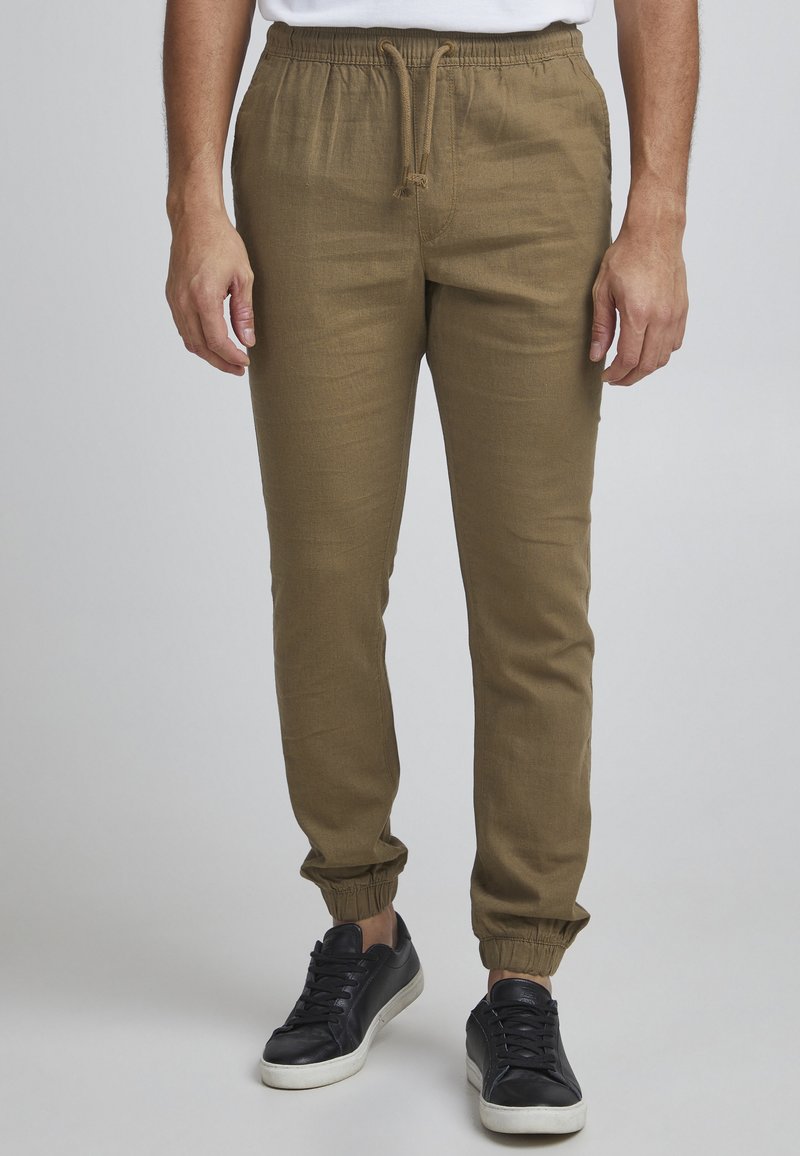 Pantalones jogger color caqui con cintura elástica, detalle de cordón y piernas ajustadas; combinados con zapatillas negras. Tejido suave y ligero.