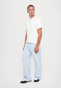 White short-sleeve t-shirt with a small logo, paired with light blue striped wide-leg trousers and black shoes. Simple and casual design.