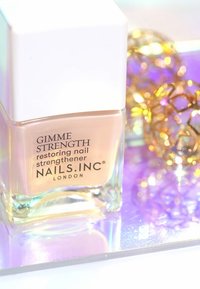 Indurente per unghie in una bottiglia di vetro trasparente con un tappo quadrato bianco. Contiene smalto beige all'interno. Il testo riporta "GIMME STRENGTH" e il nome del brand.