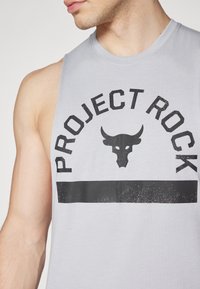 Camiseta sin mangas de color gris con un gran estampado negro de "PROJECT ROCK", acentuada por un gráfico de un cráneo de toro y una banda inferior negra sólida.