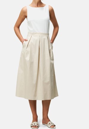 Weißes ärmelloses Oberteil kombiniert mit einem beigen, knieumspielenden, plissierten Rock mit seitlichen Taschen, getragen mit hellen Sandalen.
