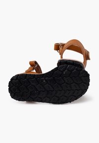 Sandalo in pelle marrone con fasce regolabili, suola in gomma nera testurizzata e design a punta rotonda. Presenta un motivo sul fondo per una buona aderenza.