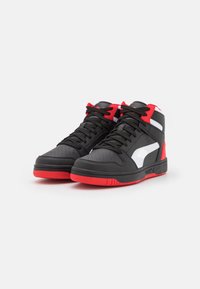 Wysokie sneakersy do koszykówki z czarnej skóry z czerwonymi akcentami. Cechy obejmują perforowany przód, białe boczne panele oraz czarne sznurówki.