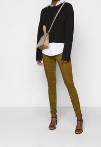 Czarny dzianinowy sweter na białej koszuli z kołnierzykiem, w zestawie z oliwkowymi wąskimi spodniami i czarnymi sandałami na obcasie. Beżowa torebka na ramię.