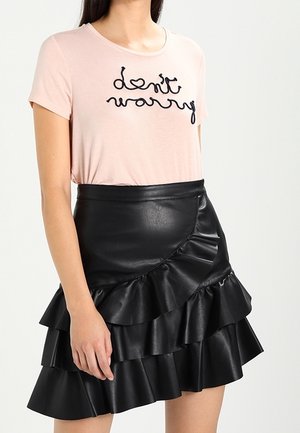 Kobieta ubrana w jasnoróżowy t-shirt z napisem „Don't Worry” oraz czarną skórzaną mini spódniczkę z falbanami w warstwach.