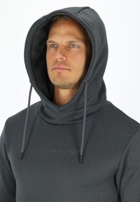 Felpa con cappuccio di un grigio scuro, con un grande cappuccio, lacci e una texture liscia. Presenta un branding minimo sul petto. Design semplice e moderno.