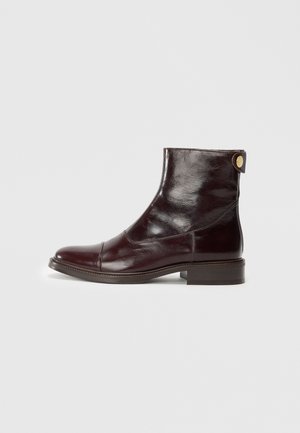 Bottines en cuir bourgogne avec un bout rond, un petit talon empilé, un col arrondi et un petit accent doré à l'arrière. Texture lisse.