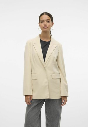 Light beige tailored blazer with textured fabric, single button closure, and two patch pockets, paired with a black t-shirt and gray wide-leg pants.
