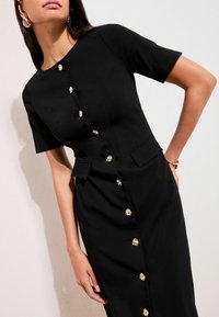 Schwarzes Kleid mit kurzen Ärmeln, verziert mit goldenen Zierknöpfen entlang der Vorderseite, strukturierten Taschen und einer taillierten Silhouette. Glatte Textur.