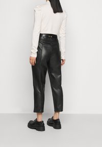 Svarta läderbyxor i cropped-modell med hög midja, slät textur, synliga sömmar och sidofickor. Kombinerade med svarta platåskor.