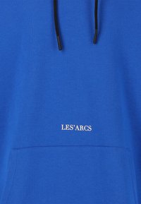 Haut à capuche bleu avec une poche avant, arborant un logo blanc "LES'ARCS". Le tissu a une texture lisse et des cordons noirs ajustables.