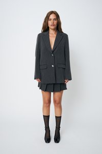 Blazer grigio a righe con chiusura a un bottone, abbinato a una gonna plissettata coordinata. Indossato con calze a rete nere e scarpe con tacco quadrato.