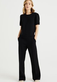 Zwarte top met pofmouwen, gecombineerd met losse zwarte wijde broek. Gladde stof met een strakke, minimalistische uitstraling. Subtiele accenten, geen patronen.