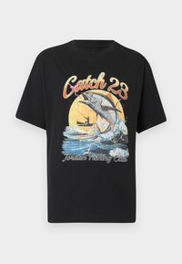 Μαύρο T-shirt με γραφικό μεγάλο ψάρι που πηδά από το νερό, ψαράς σε βάρκα, κείμενο "Catch 23" και "Jordan Fishing Club."