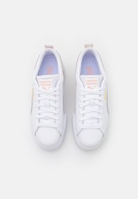 White sneakers featuring a smooth leather upper, round toe, lace closure, and pink accents on the tongue and sides. Textured rubber sole.