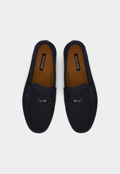 Ζευγάρι μαύρα δερμάτινα loafers με μεταλλική λεπτομέρεια στο πέλμα και καφέ εσωτερικά επικάλυψης με την επωνυμία "roberto cavalli" σε λευκό φόντο.