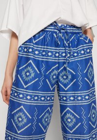 Pantalons à motifs bleus en tissu léger. Présentent des designs géométriques en blanc et bleu clair, avec une taille élastique réglable.