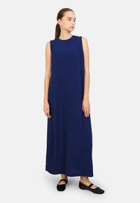 Abito maxi senza maniche di colore blu navy con scollatura rotonda, texture liscia e vestibilità comoda; abbinato a scarpe basse nere.