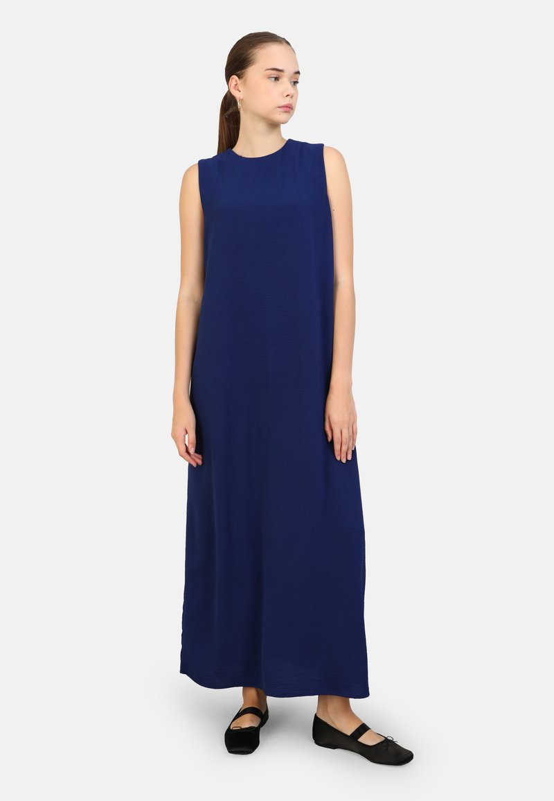 Abito maxi senza maniche di colore blu navy con scollatura rotonda, texture liscia e vestibilità comoda; abbinato a scarpe basse nere.