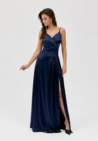 Navy saténové večerní šaty s V-výstřihem, drapovaným živůtkem a bočním rozvorem. Mají tenké ramínka a hladkou, lesklou texturu.