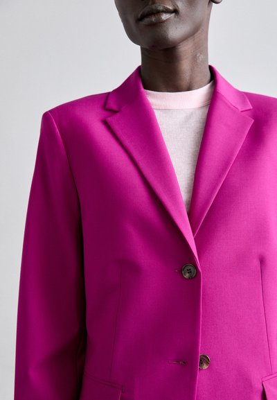 Fuksia bleiser, millel on sälguga krae, ühe nupuga kinnitamine ja küljetaskud. Kihtide kaupa kerge roosa struktureeritud t-särgi peal. Sile kangas.