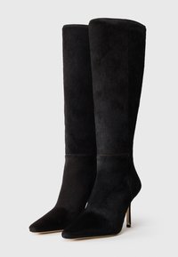 Fekete, térd fölé érő csizmák, puha, texturált anyagból készült. Hegyes orrú és vékony, magas sarkú. A varrásokkal díszített részletek vizuális érdekességet adnak.