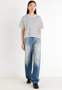 Striped white and navy t-shirt paired with light blue wide-leg jeans. Model wears black shoes; simple design with short sleeves and relaxed fit.