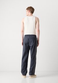 Marinewindjack broek met een elastische tailleband, zijzakken en witte zijkanten. Gecombineerd met een geribbelde witte tanktop en beige schoenen.