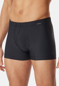 Pantaloni boxer neri con sottili righe verticali bianche, elastico in vita e un'etichetta del marchio sul lato anteriore. Tessuto morbido.