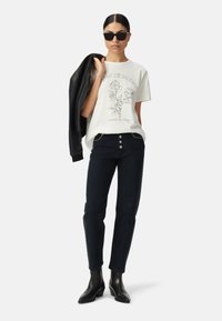 Camiseta gráfica blanca con estampado de rosa, jeans negros con tachuelas, chaqueta de cuero negra y botas negras hasta el tobillo. Modelo lleva gafas de sol negras.