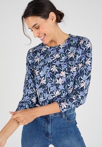 Bloemige top met lange mouwen in marineblauw met paarse en roze bladeren; zachte stof met een ronde halslijn en gathers aan de schouders.