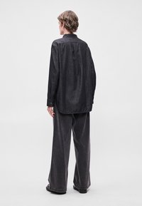 Σκουρόχρωμο τζιν πουκάμισο με μυτερό γιακά και μακριά μανίκια, συνδυασμένο με γκρίζες παντελόνες σε φαρδιά γραμμή. Απλός σχεδιασμός με χαλαρή εφαρμογή και διακριτή υφή.