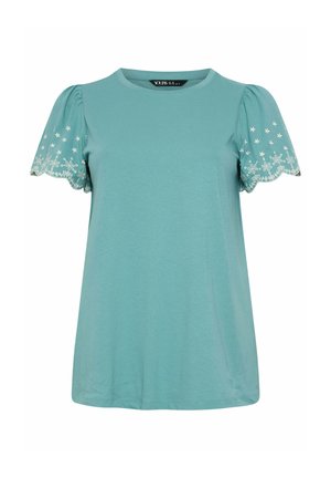 Blouse bleu clair à manches courtes avec bords de manches festonnés et broderie florale blanche sur les manches bouffantes.