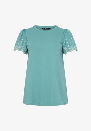 Blusa azul claro de manga corta con bordes festoneados en las mangas y bordado floral blanco en las mangas abullonadas.