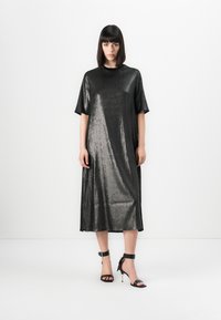 Abito midi metallico nero con maniche corte e scollatura rotonda. Texture morbida e leggera lucentezza, abbinato a tacchi neri con cinturino alla caviglia.