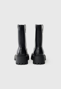 Mustad mustad nahast pahkluu saapad, millel on jämedad kummist tallad, sile tekstuur, vertikaalne õmblus ja tõmbetooted taga, et neid oleks lihtne jalga panna.