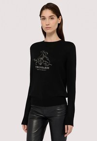 Svart tröja med långa ärmar, med en kontrasterande vit grafisk design och "Trussardi"-text på framsidan. Slät textur, avslappnad passform.