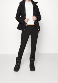 Black padded jacket with ribbed sleeves, white textured top with an orange stripe, black pants, and black snow boots with lacing detail.
