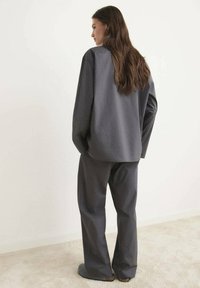 Conjunto gris de gran tamaño que consiste en una camisa de corte holgado y pantalones de pierna ancha, confeccionado con un tejido suave, exhibido en un entorno minimalista.