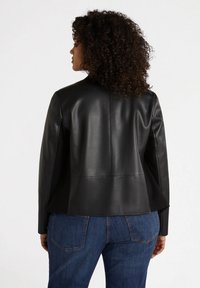 Jachetă din piele neagră cu un design structurat, mâneci de lungime medie și accente de cusătură. Pur și simplu cu blugi din denim albastru. Finisaj texturat.