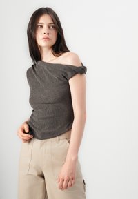 Grey ribbed off-shoulder top with rolled sleeves, paired with beige high-waisted trousers. Smooth texture and fitted design highlight the silhouette.